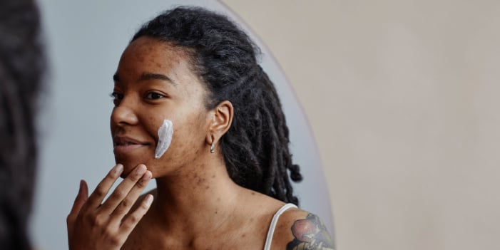 Black woman with hyperpigmentation applies professional skincare on her face.