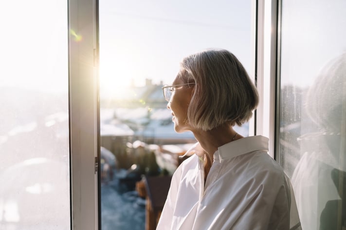 woman standing by a window in soft natural light, reflecting on skin comfort and balance