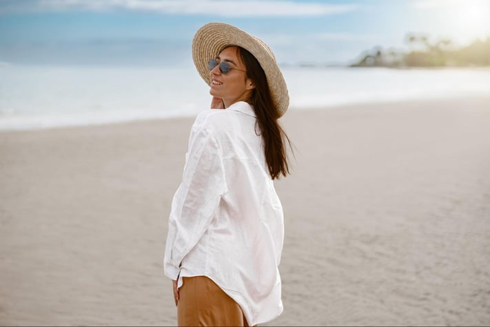 woman wearing a sun hat and long sleeve shirt to protect skin on a sunny beach