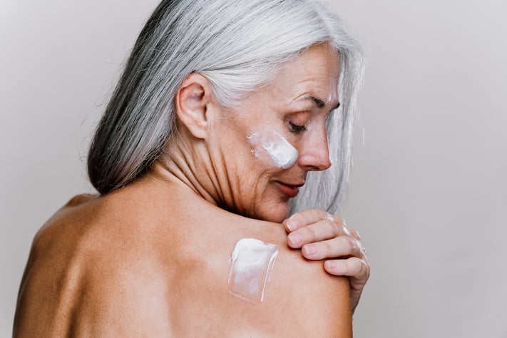 mature woman putting sunscreen onto her shoulder