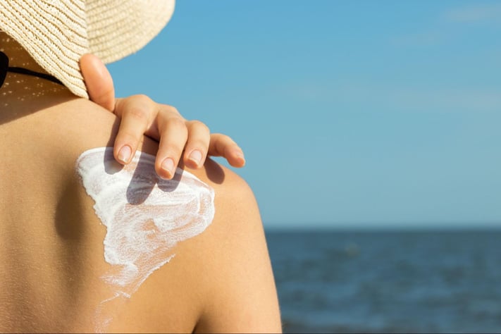 woman applying sunscreen to her shoulder at the beach