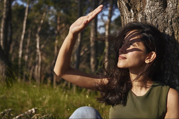 woman shielding her face from sun exposure, a common rosacea trigger