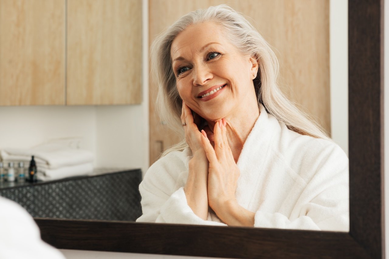 mature woman looking at her healthy skin in the bathroom mirror