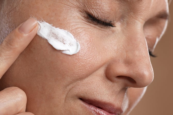 woman applying moisturizing cream to her cheek as part of a hydrating skincare routine
