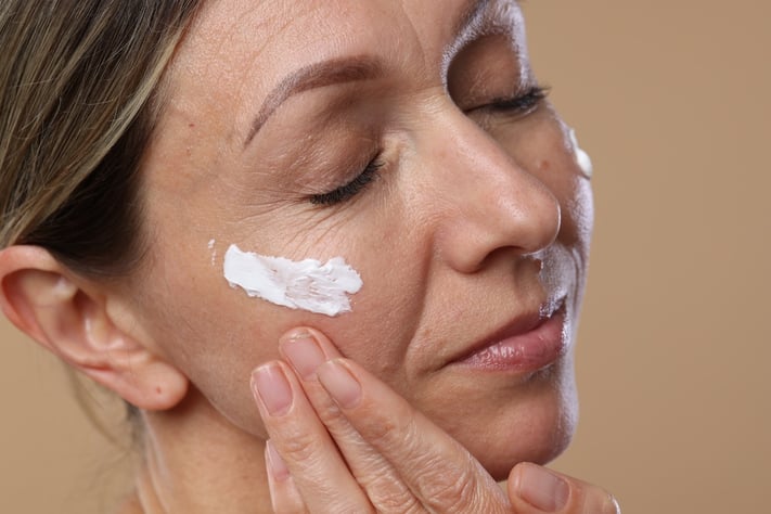 mature woman applying moisturizer with spf
